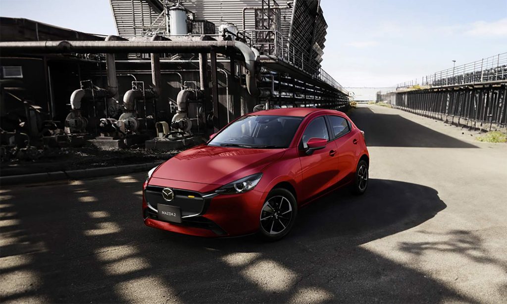 Mazda 2 Hatchback 2024 en México - color rojo, nuevo frente con parrilla en color negro y faros LED con encendido automático, estacionado en ciudad